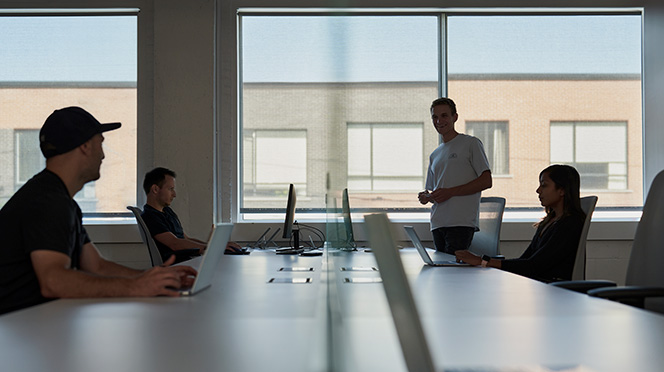 Four young venture scientists gathered around a table with their laptops, engaged in discussion.